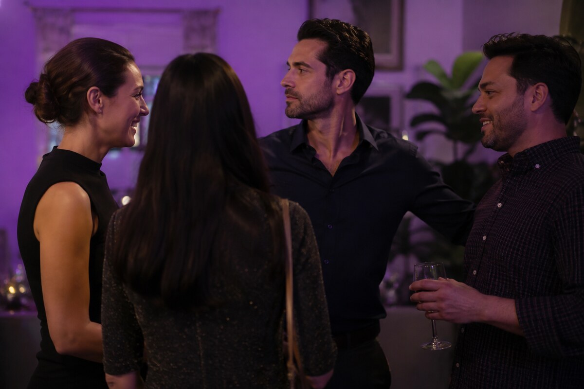 A woman being introduced at a social gathering while a man appears emotionally distant